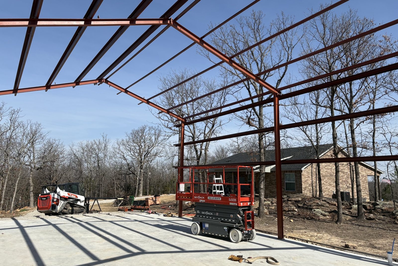 Red steel building frame standing on a concrete slab under a blue sky